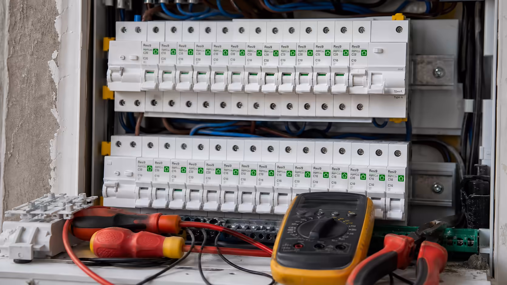 Outils d'électricien posés sur un tableau électrique ouvert avec disjoncteurs Schneider Resi9 et différentiels 30 mA type A en vue rapprochée